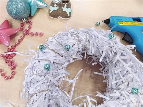 Изготовим новогодний венок из бумажной стружки и украсим его елочными украшениями.
